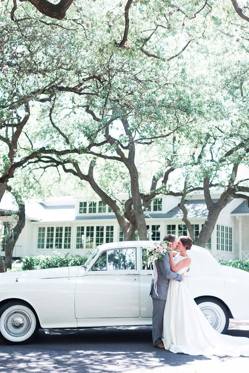 wedding couple standing besides white bently car 