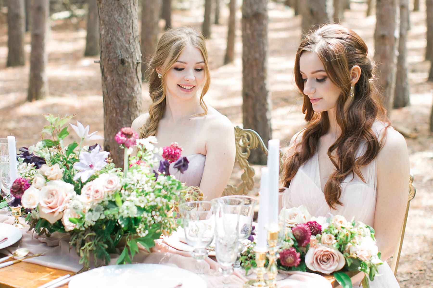 two brides maids sitting at the table with flowers and candles in the nature 