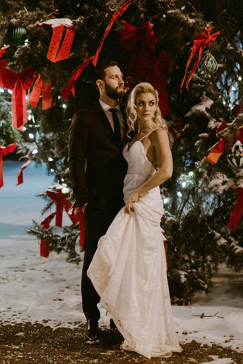 happy bride and groom standing under Christmas tree outdoors 