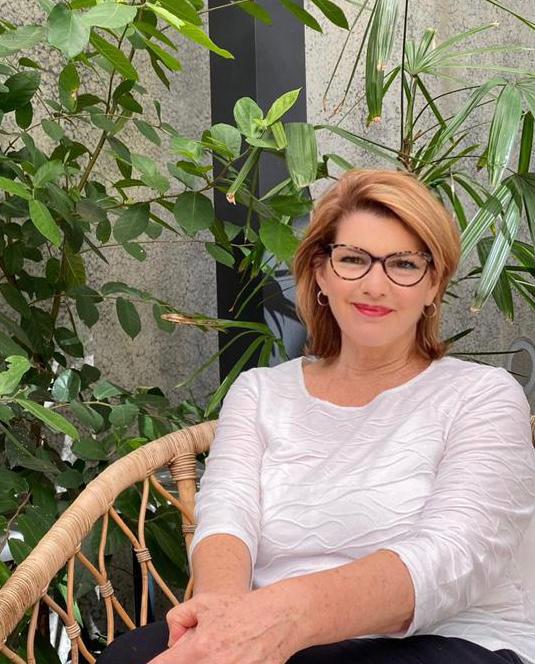 Beauty therapist sitting on a chair with palms in the background.