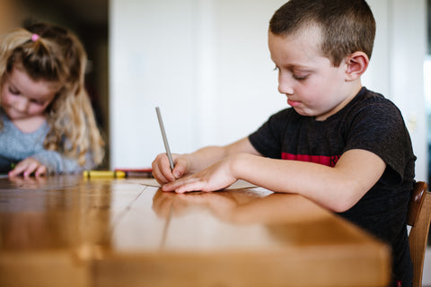 elementary age boy sitting at an oak table with pencil and paper in hand