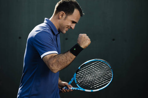 Tennis player in the middle of doing a victory arm pump. He is wearing Bauerfeind's Sports Wrist Strap to help prevent his forearm muscles from fatiguing and developing into tennis elbow. 