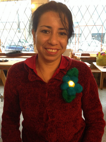 a female Scout Leader with dark hair in a ponytail smiles wearing a maroon zip up shirt. She is wearing an led badge shaped like a flower with a light in the centre.
