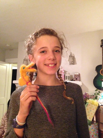 a young gil wih light skin and curly blond hair holds up a felted seahorse she felted for a baby mobile