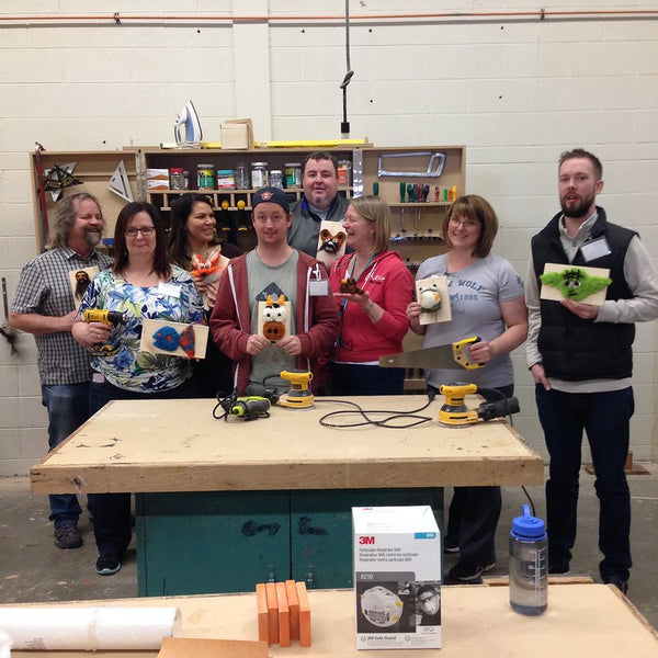 a group of teacher stand in a workshop holding up their felted creatures on a plaque project