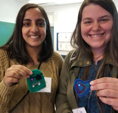 Two teachers hold up 2D felted wool badges with led lights on them.