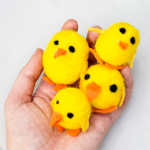 a close up of a hand holding 4 yellow easter chicks with orange beaks and feet shaped like triangles