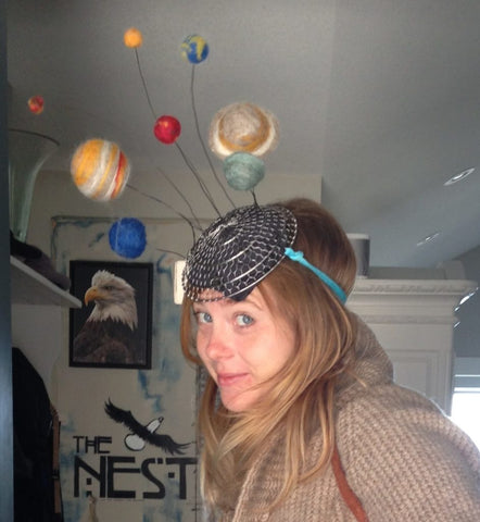 a ginger haired light skinned woman (Emily Smith) wear a hat with felted planets attached with wires like antenaes