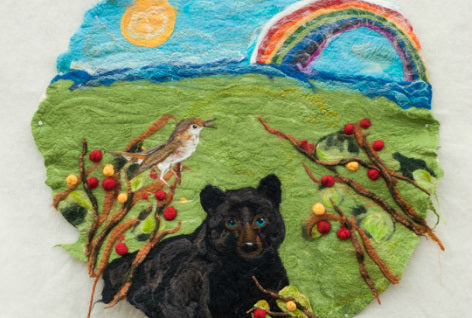 Wet felted meadow scene from the book Taan's Moon. A bear sits in the foreground and a rainbow in a blue sky