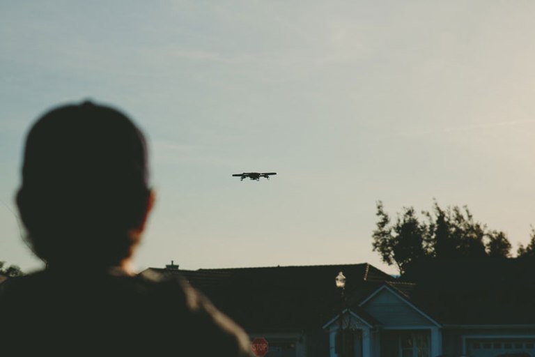 Man in baseball cap watching drone fly by at sunset in a neighborhood