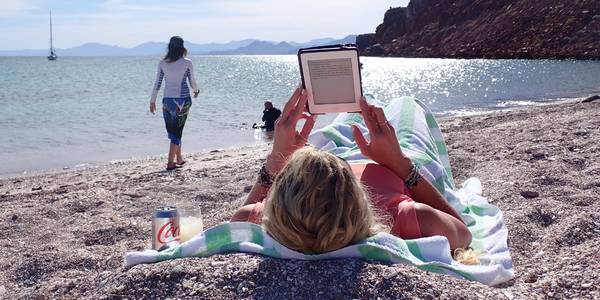 woman lying on her back on the beach reading a kindle