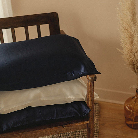 Trois oreillers avec une taie d'oreiller en soie Emily's Pillow sont sur une chaise en bois