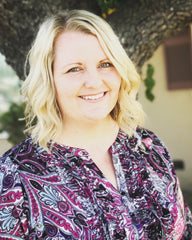 Photo of smiling Rachel in a purple blouse standing in front of a tree.