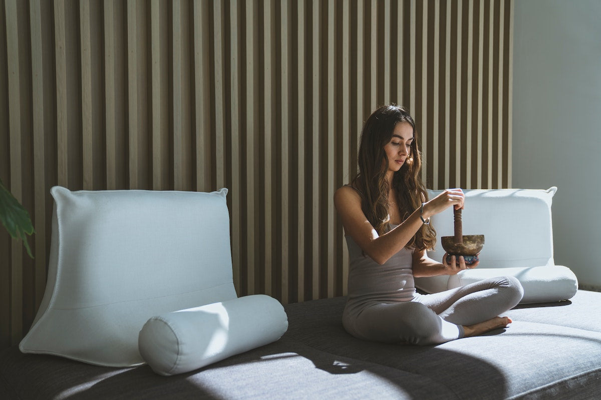 Lady sitting cross-legged on her mattress fiddling with a tibetan song bowl