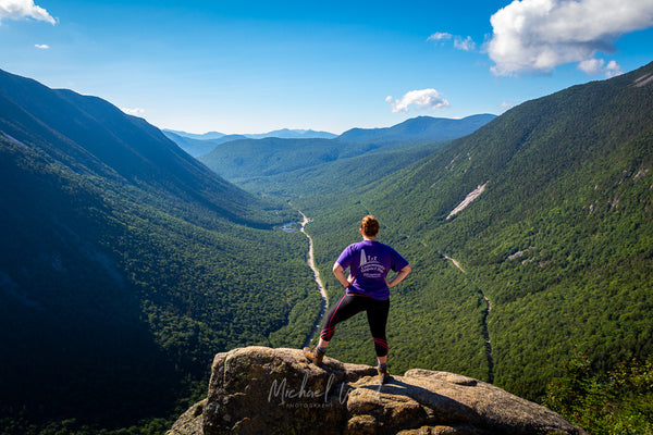 A hiker stands on top of a boulder looking out at Crawford Notch in the White Mountains of New Hampshire