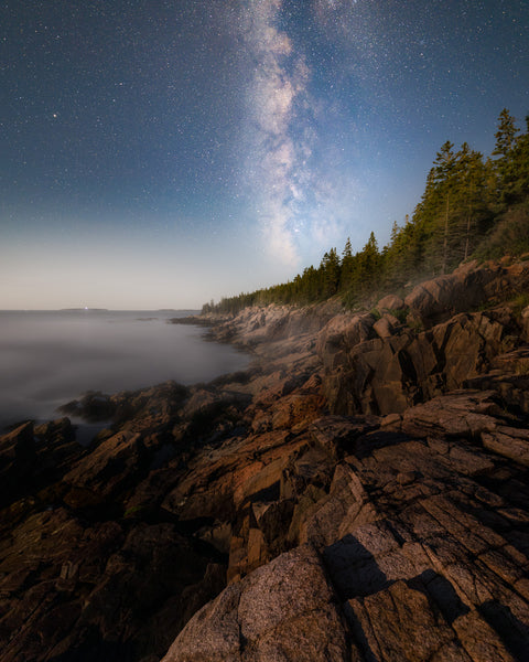 A faint Milky Way positioned vertically over the rocky shoreline of Acadia National Park in Maine