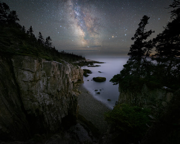 The Milky Way dominates the night sky, looking down at a pebble beach at The Raven's Nest in Acadia National Park, Maine