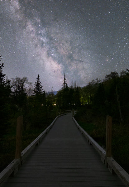 The Milky Way galaxy in the night sky rising over a boardwalk in the forest of Vermont