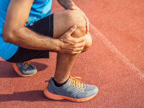 runner on track field holding knee due to pain