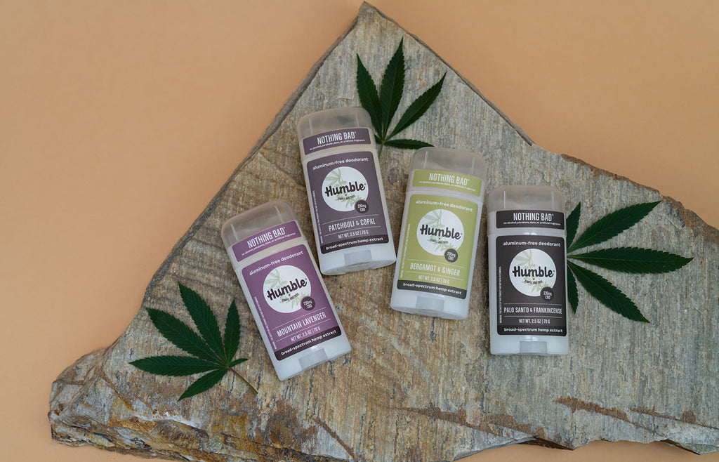 Four CBD deodorants with hemp leaves on a stone