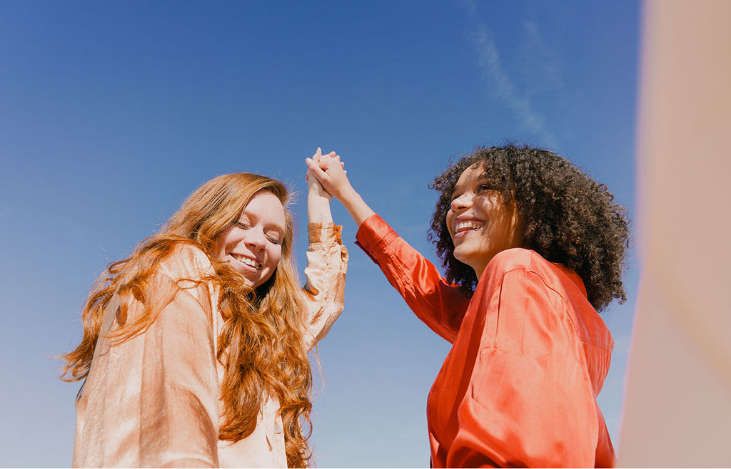 Two women holding hands and smiling with blue sky in background