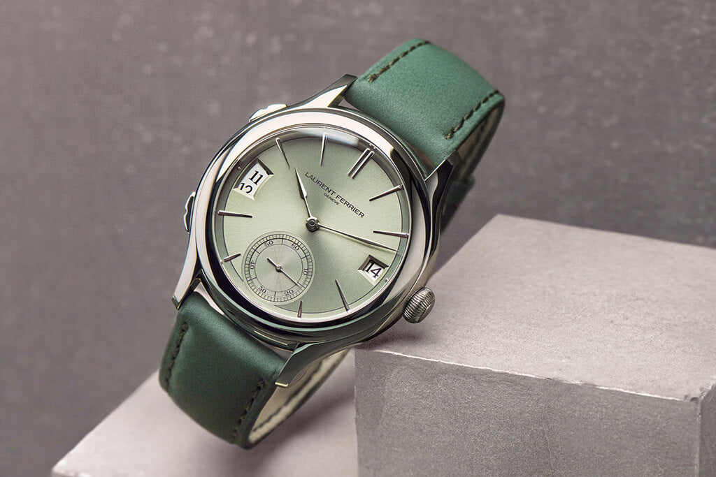 Magnetic green dial watch from swiss fine watchmaker Laurent Ferrier Geneva, it is resting on a concrete cube. The watch features a green lime reflective dial, white-gold assegai hands and indexes and dual-time date windows.