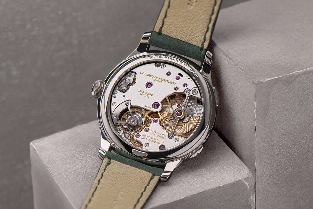 Watch resting on its front on two steps-like concrete blocs exposing the "Série Atelier III" engraving at the top of the back case as well as the LF230.02 Traveller highly hand-finished movement