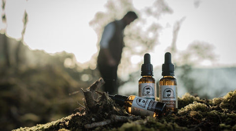Silhouette of bearded man in nature with beard oil bottles in the foreground