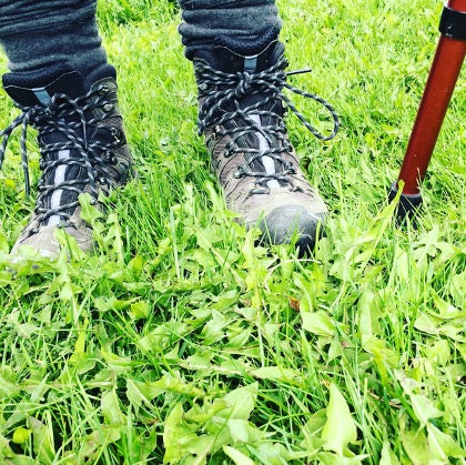 A pair of brown and black hiking boots on green grass with added protection from wearing waterproof socks during a hike.