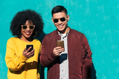 A smiling couple wearing sunglasses holding refurbished phones in their hands