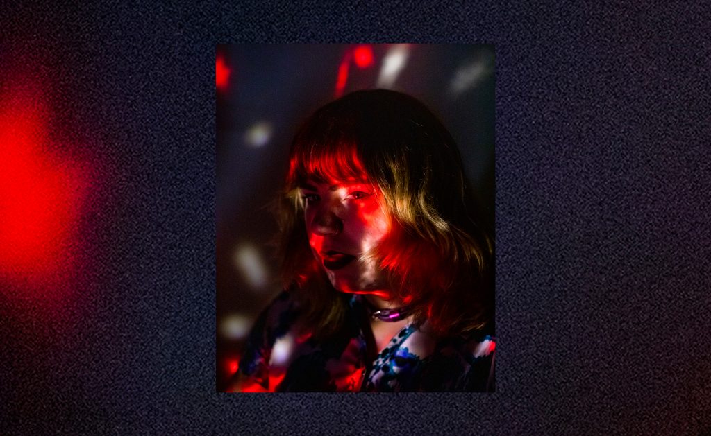 Portrait of Marbie Miller in a dark room with colorful lights highlighting her face.