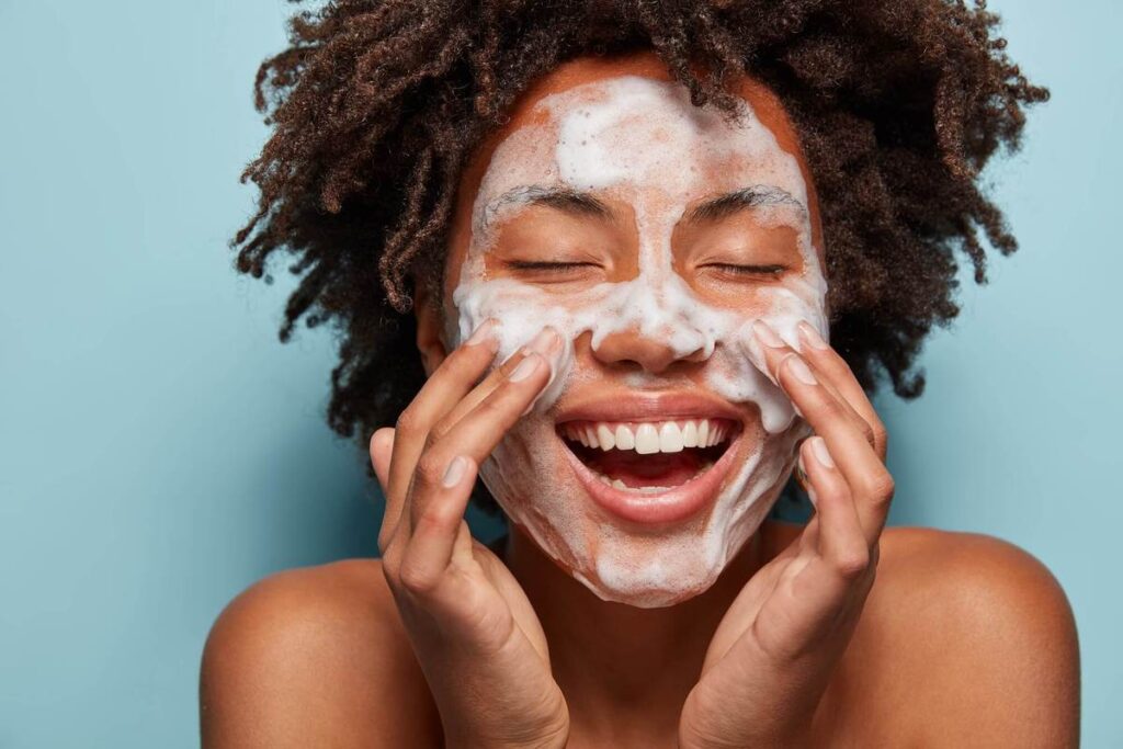 curly haired woman applying beauty cream to her face while smiling