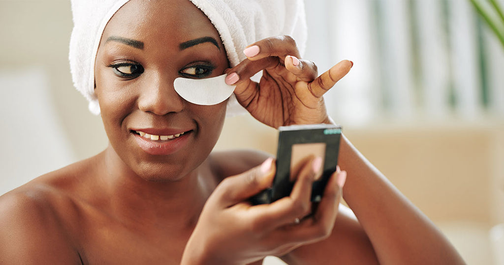 black woman put cococumber to her eyes while she stares at the mirror