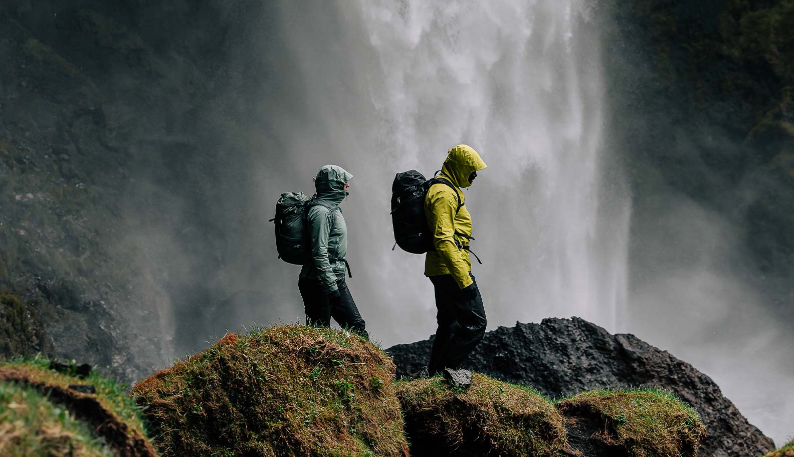 two-people-in-phase-lite-jackets-walking-under-waterfall