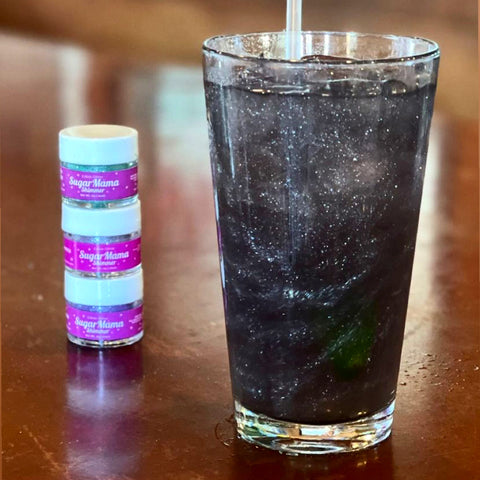 Black Edible Glitter in clear soda in pint glass with three 4-gram jars of Sugar Mama Shimmer Edible Glitter for Drinks. 