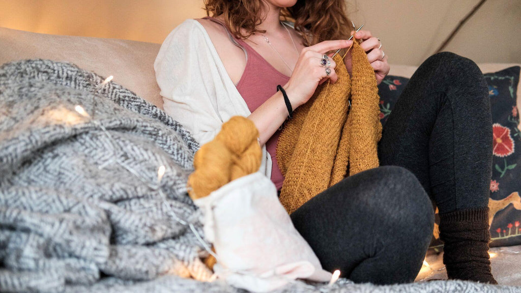 Woman knitting a scarf on the sofa