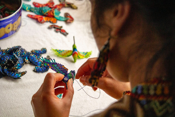 Inga Artisan sews on the wing of a Hummingbird Ornament
