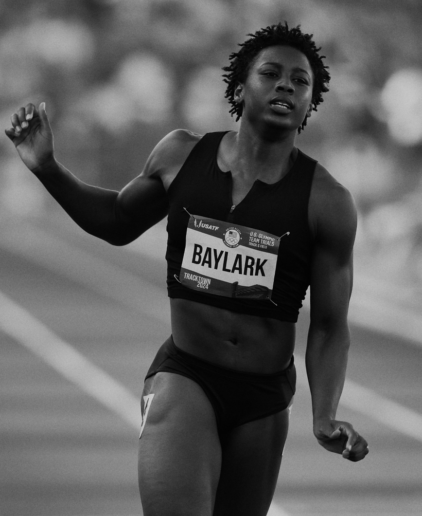 Runner with 'BAYLARK' name tag in mid-stride at a track event.