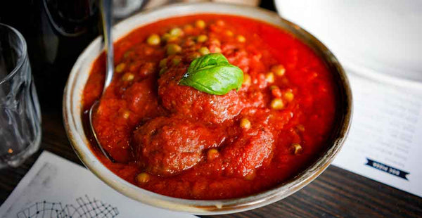 Fresh tomato sauce in bowl with spoon and basil leaf on top