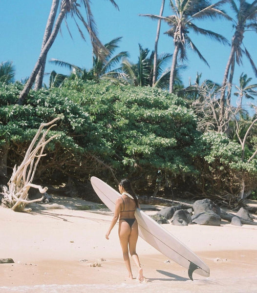 Makoa carrying her surfboard on the beach
