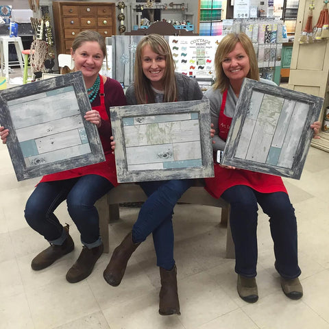 3 women in red aprons holding up decorated picture frames