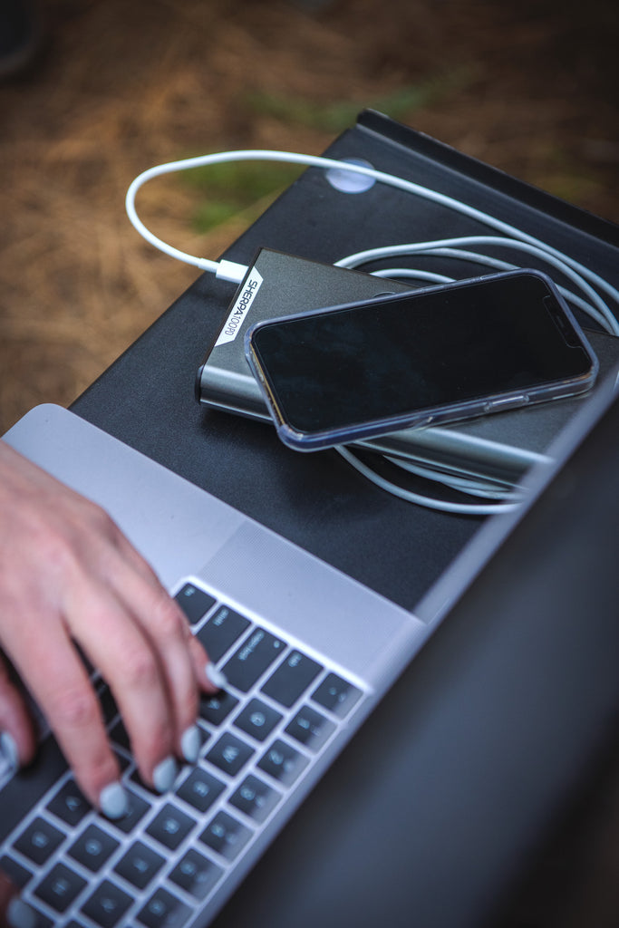 Goal Zero Sherpa 100PD Portable Power Bank powering an Apple laptop with a cable and and iPhone wirelessly.