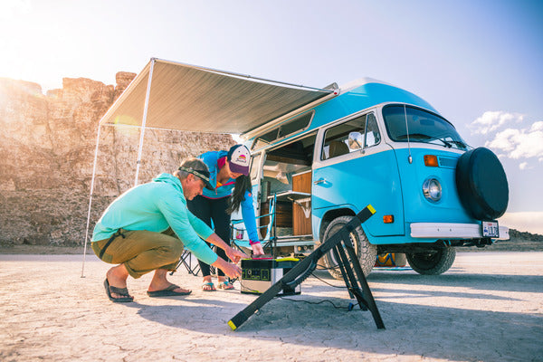 Two people set up a Goal Zero solar generator outside a van in the desert.