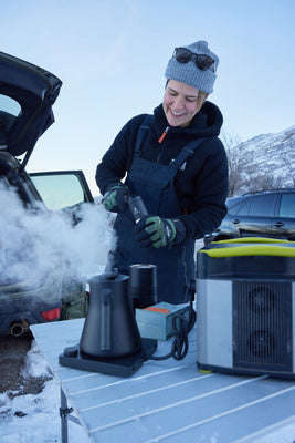 A person makes coffee while camping with gear plugged in to a Goal Zero portable power station