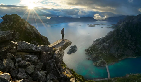 Norrona Welcome to Nature a man standing on an outcropping above the fjords in Norway