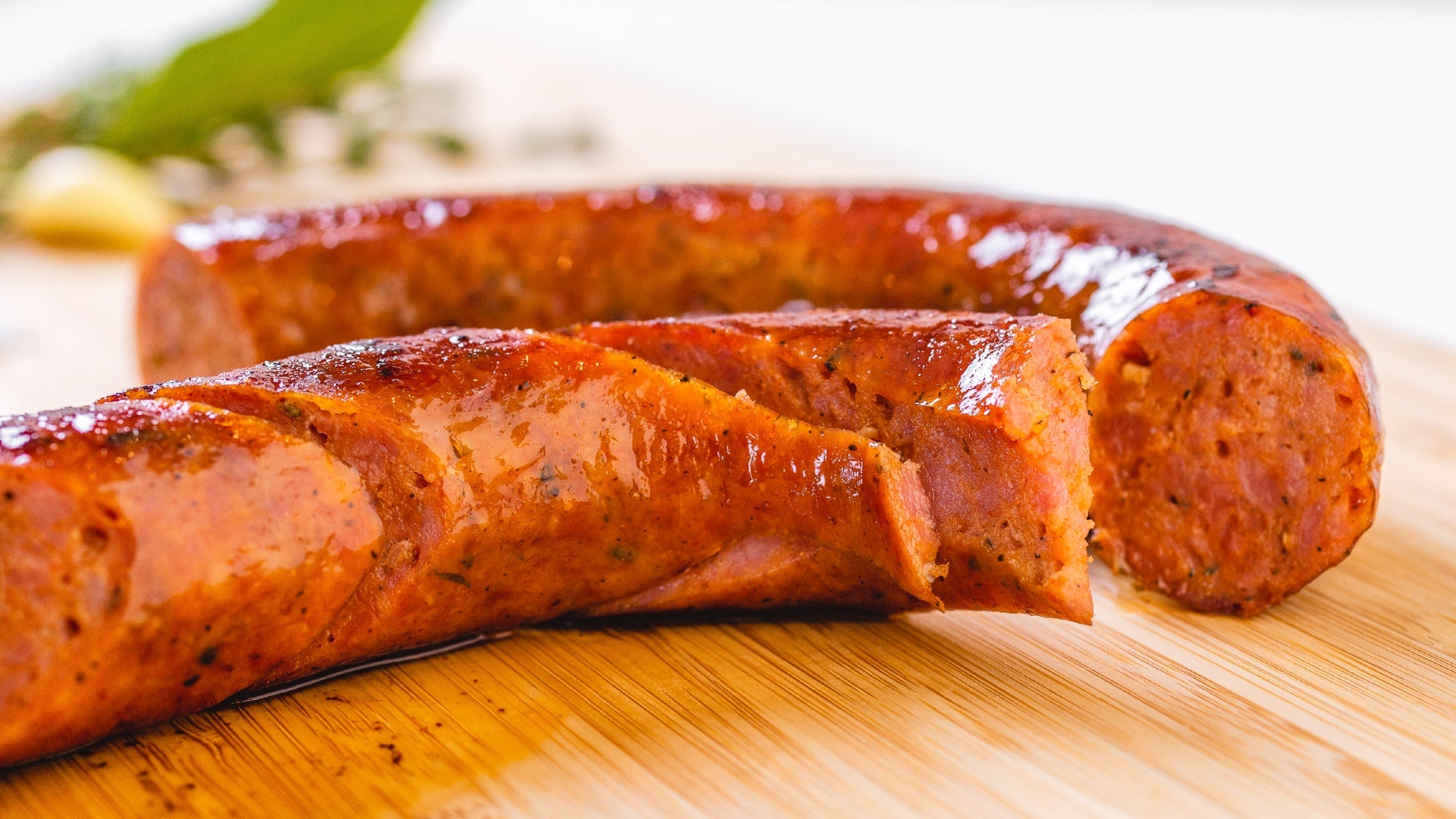 A close up of Andouille sausage on a cutting board. Half of the sausage is cut into slices and the other half remains whole.