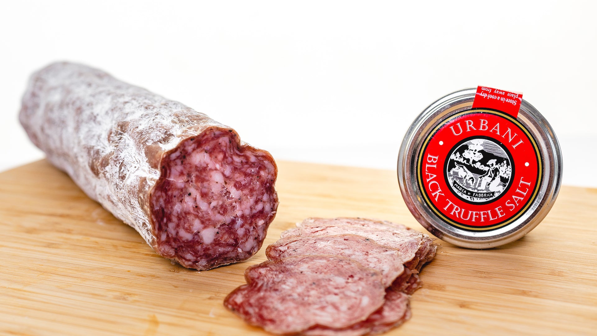 Black truffle salami on a cutting board with the cut end facing the camera and several slices of salami in the foreground.