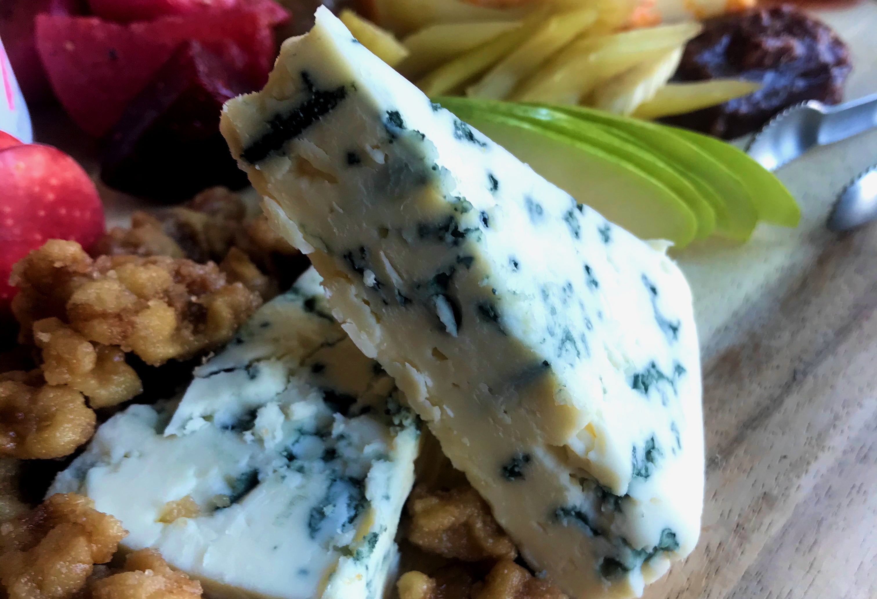 A close up picture of blue cheese on a charcuterie board surrounded candied walnuts and accompaniments. 