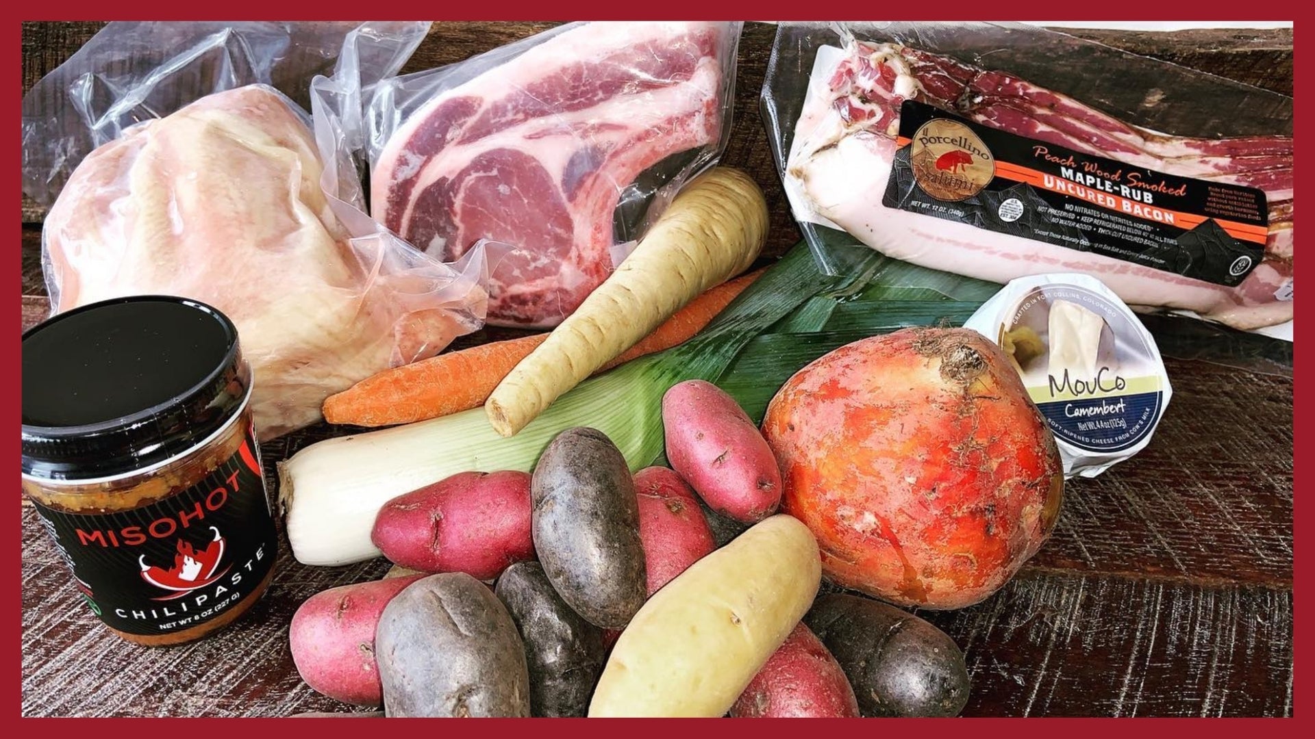 A picture of vegetables, meat, cheese and canned goods on a wood table.