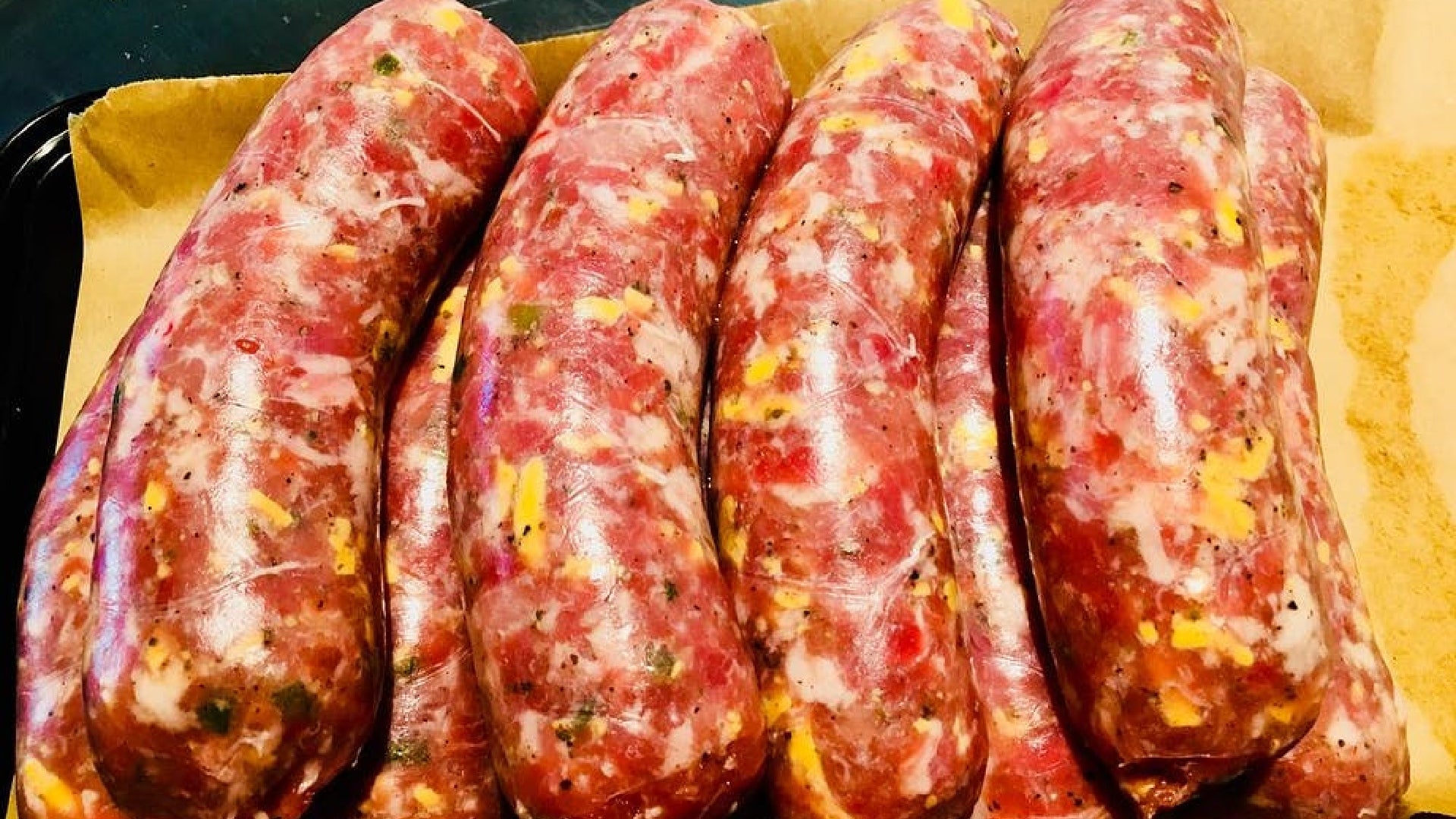 A picture looking down at several uncooked cheddar sausages stacked on top of each other on parchment paper.